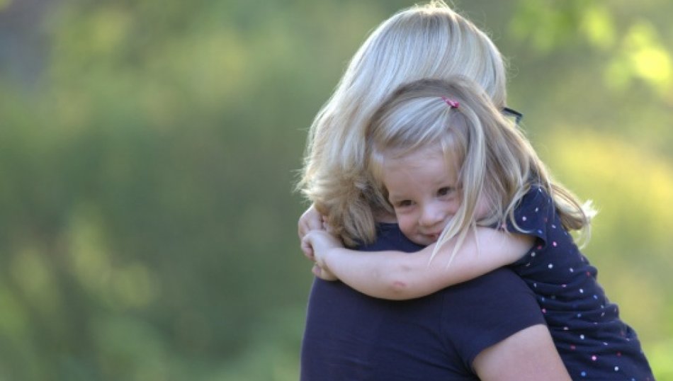 Vertraute Umarmung zwischen Mutter und Kind Kleines Mädchen umarmt seine Mutter innig im Grünen
